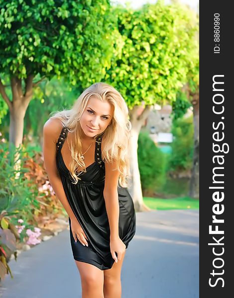 Beautiful blonde girl in black dress in summer garden