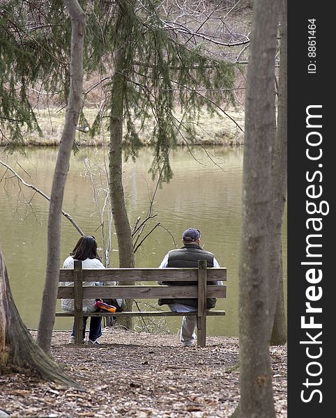 Heterosexual couple sitting on wood bench near pond. Heterosexual couple sitting on wood bench near pond