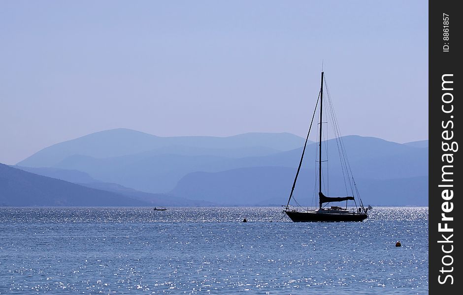 A blue sea landscape with a sailboat silhouette. Tolo, Peloponnese, Greece. A blue sea landscape with a sailboat silhouette. Tolo, Peloponnese, Greece.