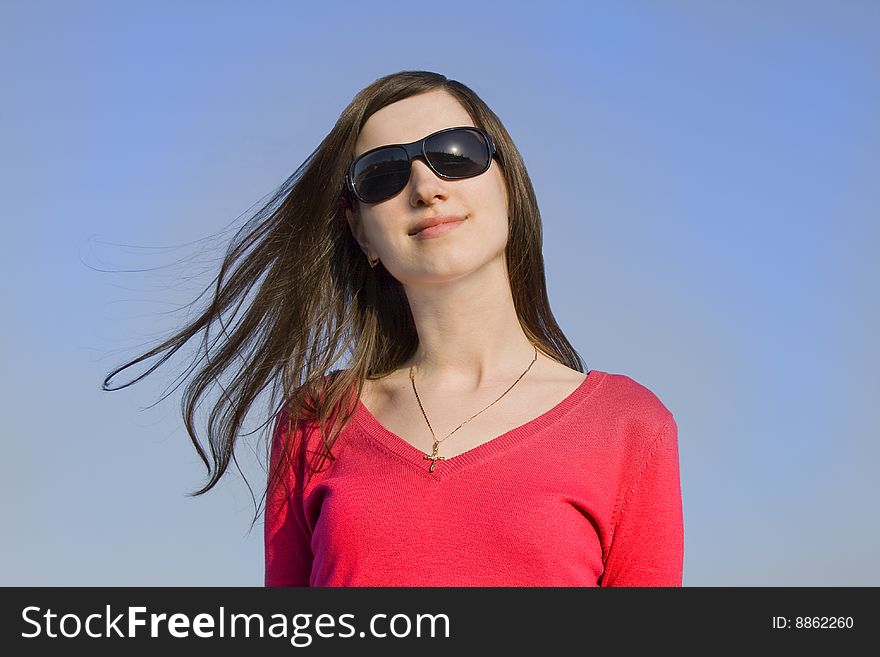 Closeup portrait of a beautiful young woman in sunglasses over big blue sky