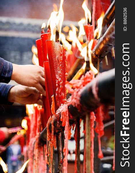 A picture of burning long red burning candles and a pair of male hands holding a candle in chinese tample