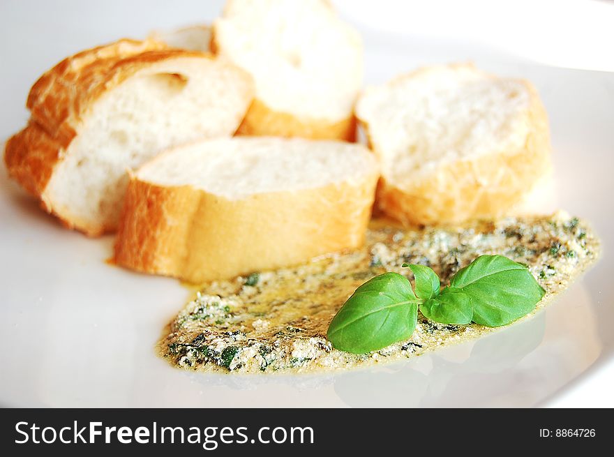 Pesto sauce and four slices of baguette, garnished with basil leaves, served on a white plate.