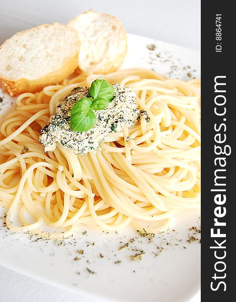 Spaghetti with pesto sauce and two slices of baguette, garnished with herbs, served on a white plate.