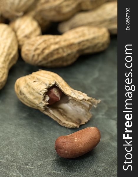 Peanuts on green marble background, one opened peanut in focus, distance blur