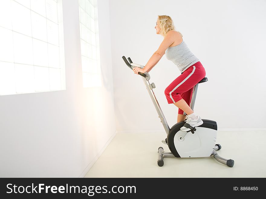 Woman dressed sportswear exercising on spinning bike. She's smiling and looking at camera. Woman dressed sportswear exercising on spinning bike. She's smiling and looking at camera.