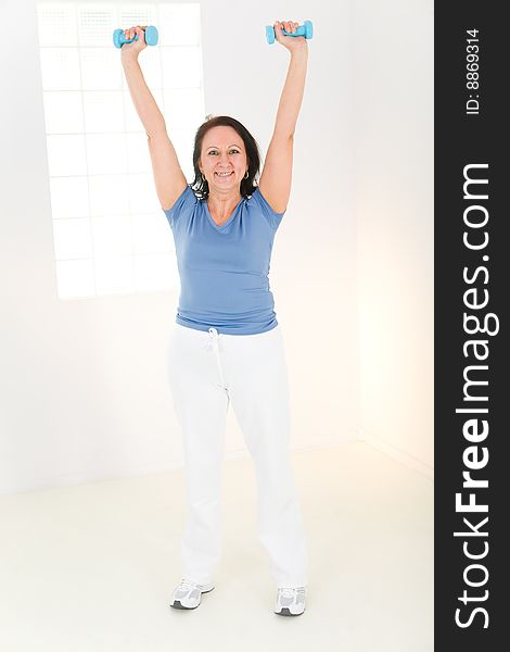 Elder woman exercising with dumbbell. She's smiling and looking at camera. Front viev. Elder woman exercising with dumbbell. She's smiling and looking at camera. Front viev.