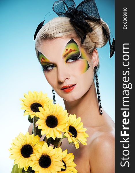 Young beauty with butterfly face-art and bouquet of sunflowers