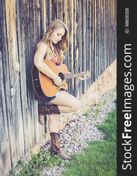 Woman Playing Guitar While Leaning On Wood During Daytime