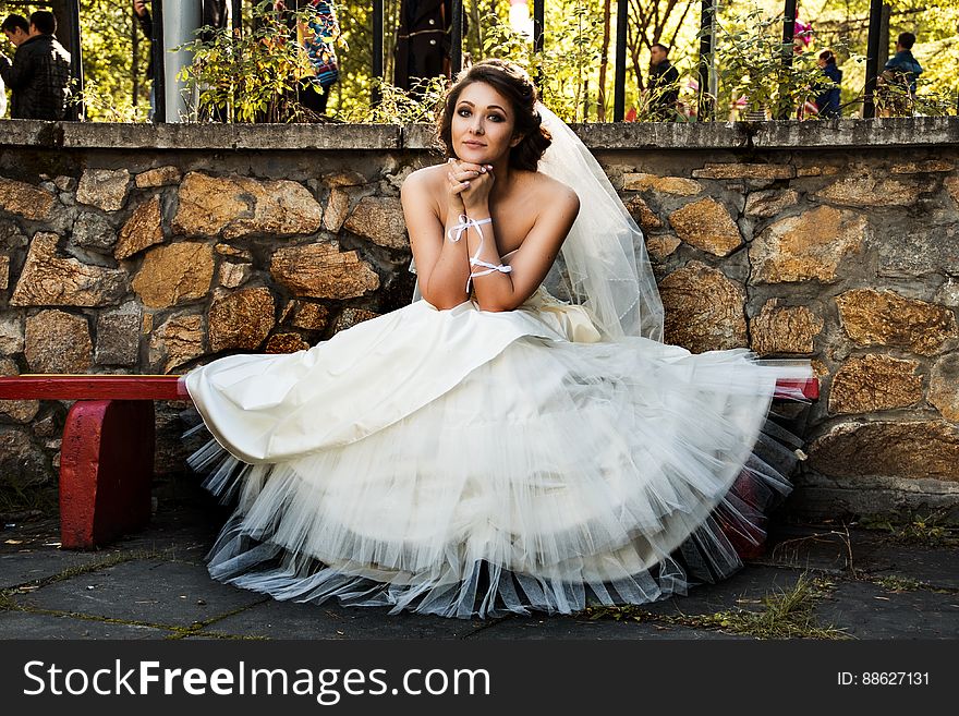 A woman in bridal gown sitting on a bench in the yard. A woman in bridal gown sitting on a bench in the yard.