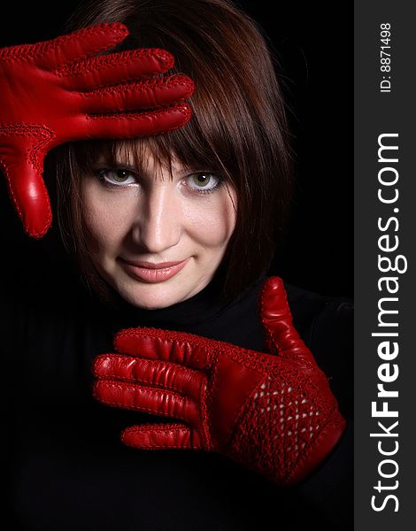 Woman looking straight from dark. In front of her red gloves on her hands. Vertical