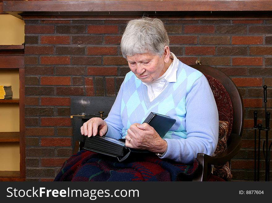 One elderly adult female sitting in a chair near the fireplace looking at a photo album. One elderly adult female sitting in a chair near the fireplace looking at a photo album