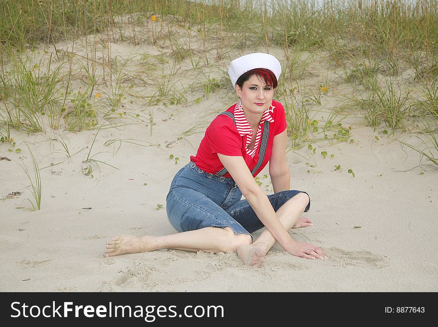 One pretty woman in red white and blue nautical wear posing on the beach near a dune. One pretty woman in red white and blue nautical wear posing on the beach near a dune