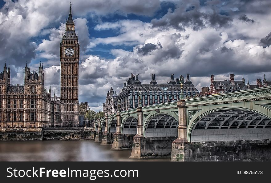 Big Ben and House of Commons viewed from Westminster Bridge showing the arches over the River Thames, London, interesting clouds and sky.