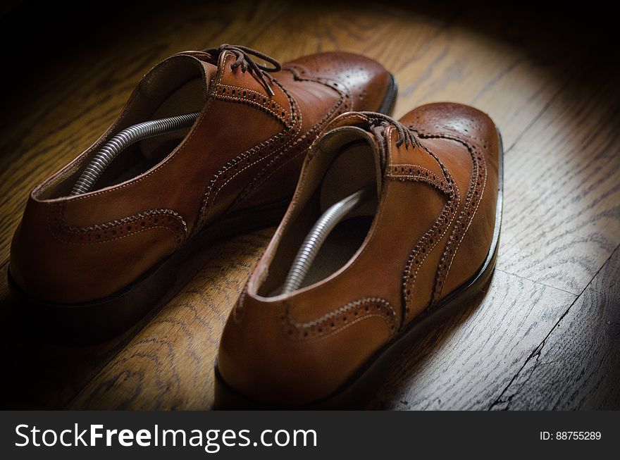 Pair of fashionable brown leather brogue shoes with shoe trees in them, grainy wooden background.