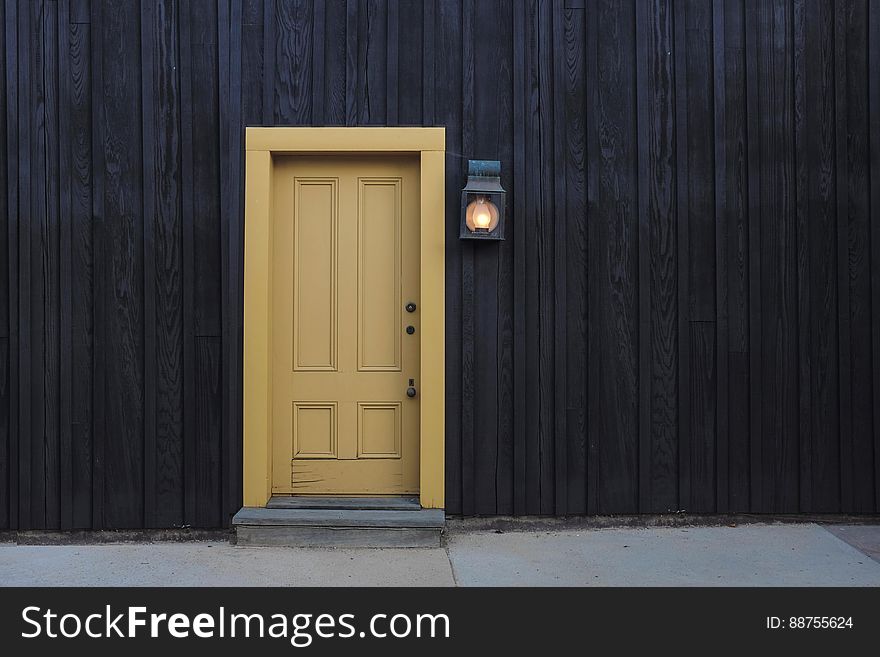 Black painted wooden house with paneled yellow (beige) painted door, blue slate step and gray path alongside. Black painted wooden house with paneled yellow (beige) painted door, blue slate step and gray path alongside.