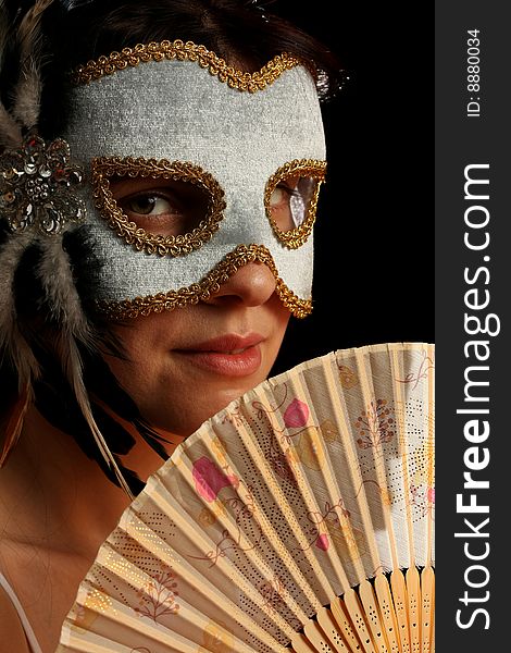 Young brunette with venetian mask and spanish fan, on black