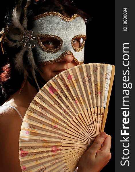 Young brunette with venetian mask and spanish fan, on black