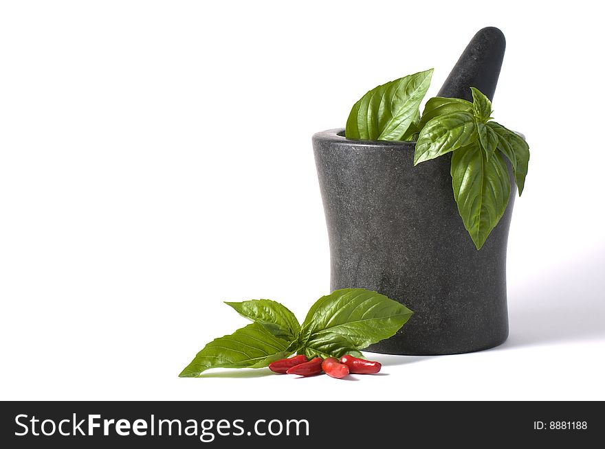 Fresh basil and chlli in a mortar and pestle against a white background from above. Fresh basil and chlli in a mortar and pestle against a white background from above