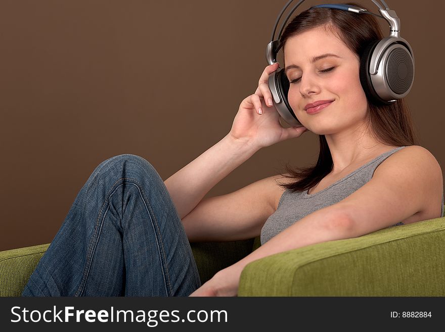 Young brown hair woman listening to music sitting on green armchair. Young brown hair woman listening to music sitting on green armchair