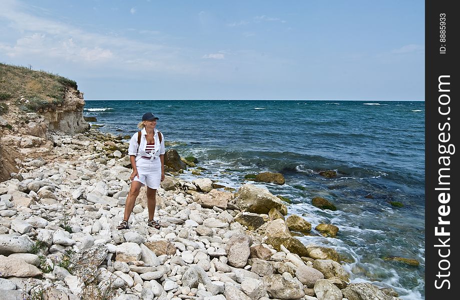 A happy smiling woman is standing on the rocky seashore looking at sea. A happy smiling woman is standing on the rocky seashore looking at sea