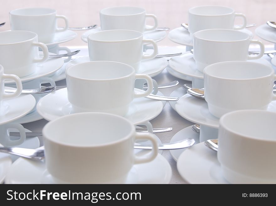 White coffee cups and saucers arranged in rows. White coffee cups and saucers arranged in rows