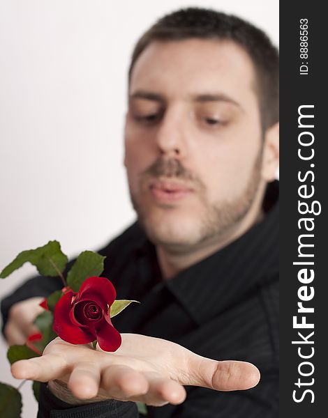Young man, holding a beautiful red rose on his open palm, blowing in its direction. Young man, holding a beautiful red rose on his open palm, blowing in its direction