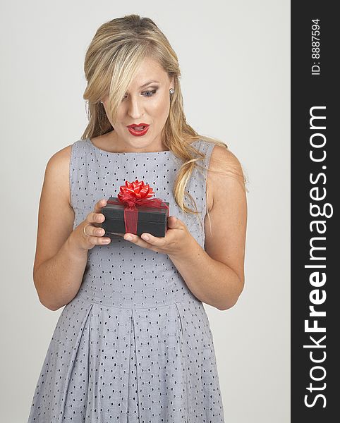 Portrait of a beautiful blonde woman with light blue eyes and classic make-up holding a gift box with excitement on grey background. Portrait of a beautiful blonde woman with light blue eyes and classic make-up holding a gift box with excitement on grey background