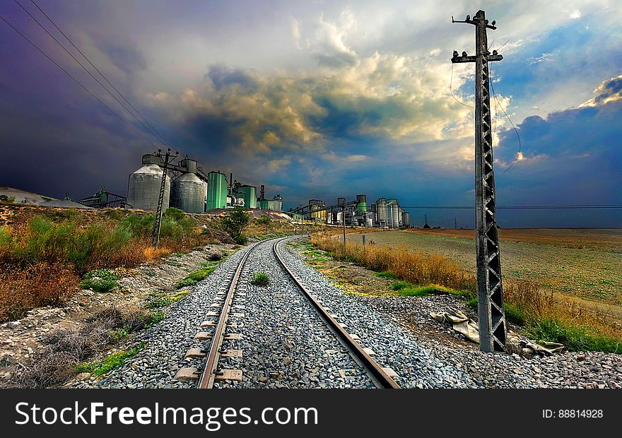 Scenic view of curving railway track receding past industrial engineering plant with towers and silos. Scenic view of curving railway track receding past industrial engineering plant with towers and silos.