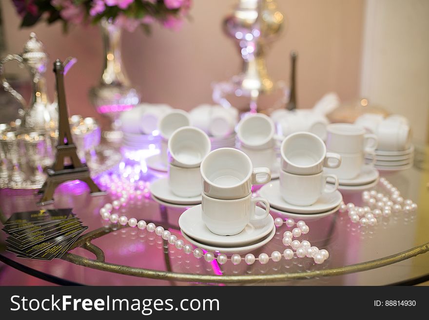 Ornamental tea set on glass table at wedding reception with model of Eiffel tower, flowers beads.