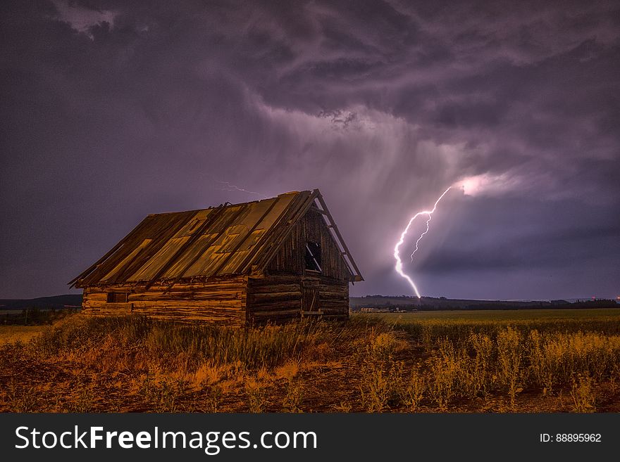 Brown and Beige Wooden Barn Surrounded With Brown Grasses Under Thunderclouds