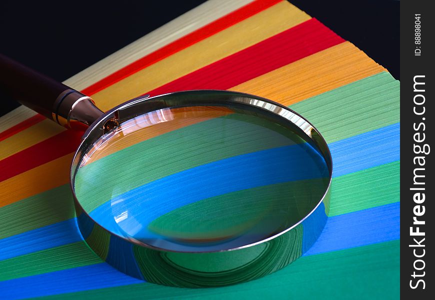 A fan of colorful sheets of papers and a magnifying glass on top. A fan of colorful sheets of papers and a magnifying glass on top.