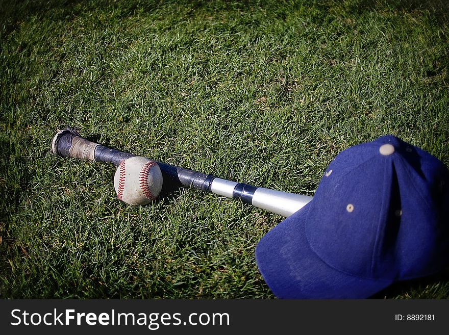 A baseball and a bat and hat on a grassy baseball field. Tilt shift lens used. A baseball and a bat and hat on a grassy baseball field. Tilt shift lens used