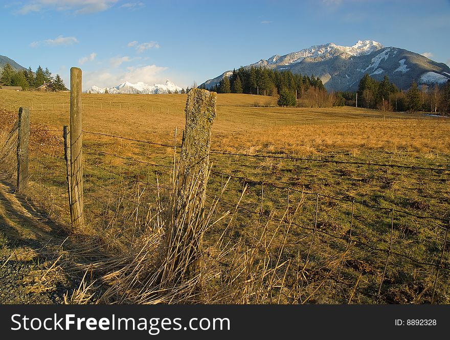 A scenic view of snow covered mountains from a fenced rural pasture