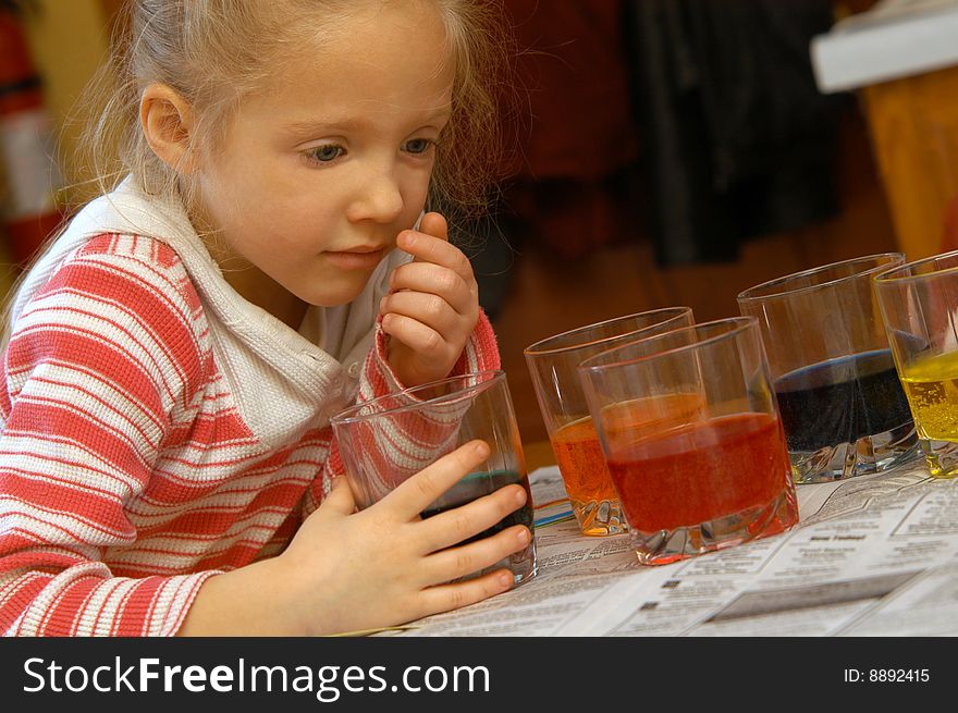 A young girl examins one of the many glasses at her table with colorful liquid in them. A young girl examins one of the many glasses at her table with colorful liquid in them.