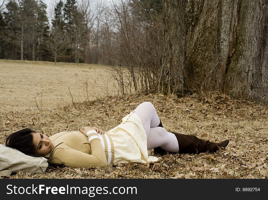 Young Indian girl is lying down next to a tree in fall. Young Indian girl is lying down next to a tree in fall.