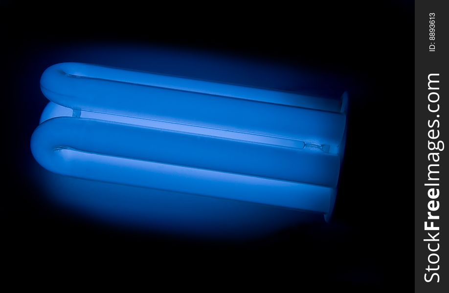 Energy saving lamp (light bulb) with dark blue colour on the black background. Energy saving lamp (light bulb) with dark blue colour on the black background