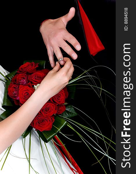 Hands over wedding bouquet with rings on black background, studio shot