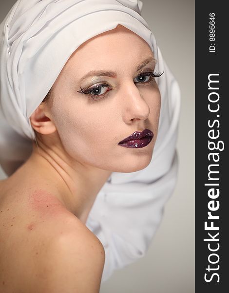 Portrait of the beautiful young woman with a bright make-up and a white fabric on a head