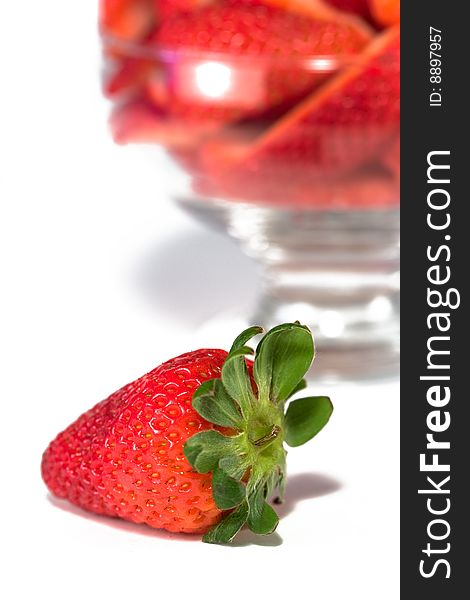 Isolated strawberry in front of bowl of cut strawberries. Isolated strawberry in front of bowl of cut strawberries.