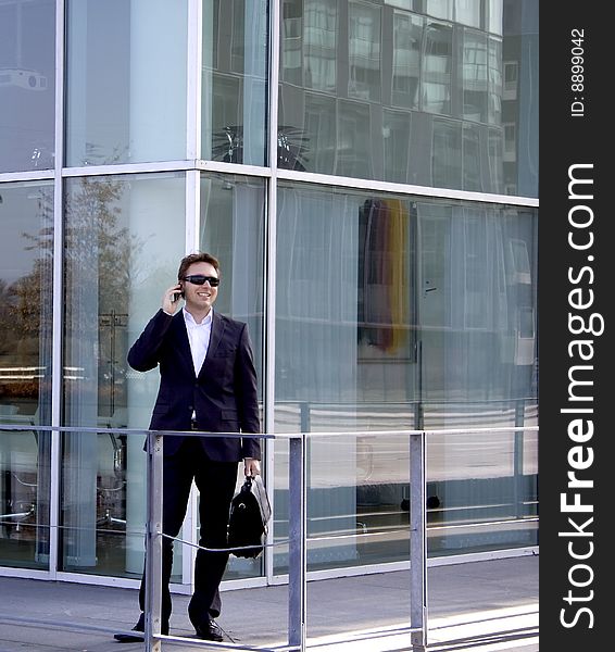 A young business man is speaking on the cell phone outside an office building of glass. A young business man is speaking on the cell phone outside an office building of glass.