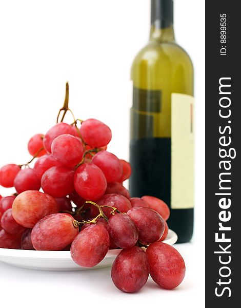 Bunch of red grapes on white plate beside wine bottle. Bunch of red grapes on white plate beside wine bottle.