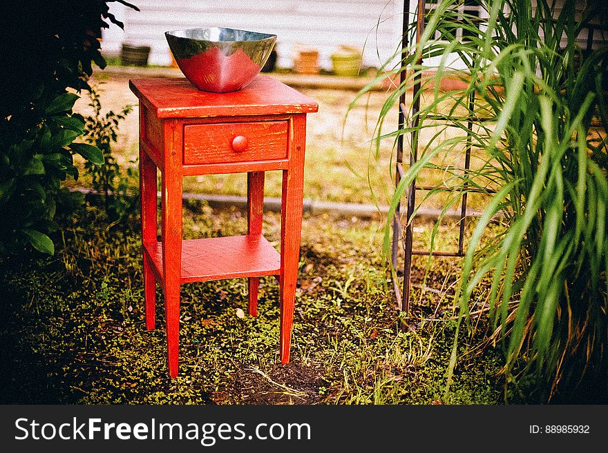 A red console table with a metal bowl in the garden. A red console table with a metal bowl in the garden.