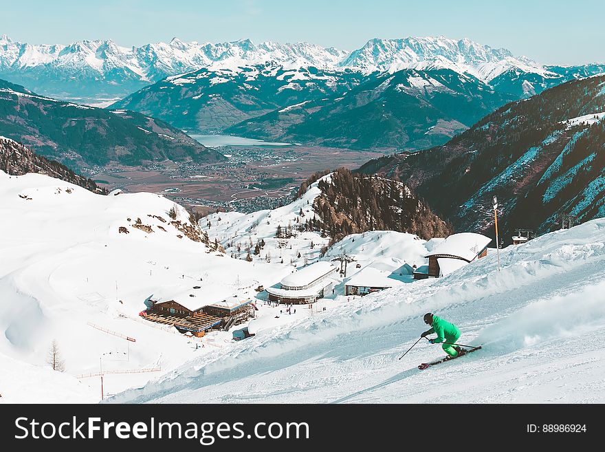 Skier on alpine slopes with resort in valley and mountain lake in horizon on sunny day. Skier on alpine slopes with resort in valley and mountain lake in horizon on sunny day.