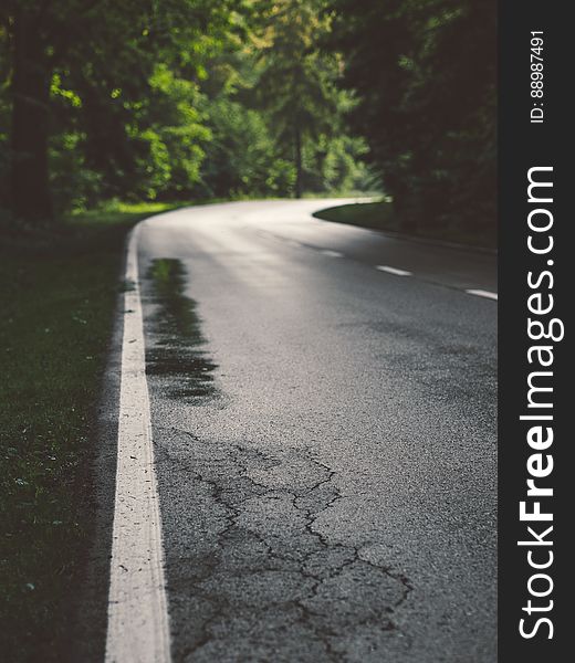 Low angle view of curving road in countryside with cracked asphalt.