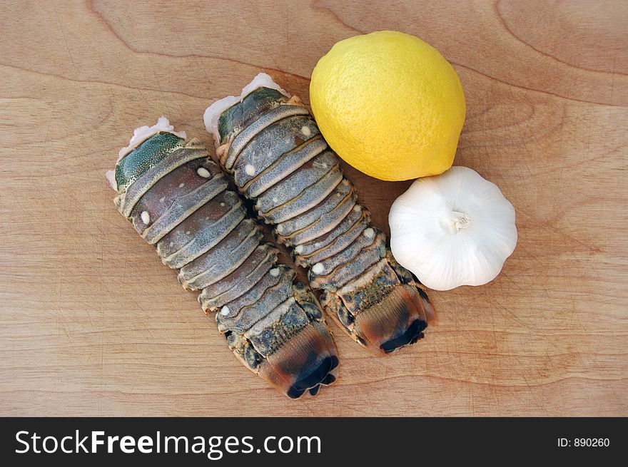 Delicious lobster tails with ripe lemon and sweet garlic on a wooden cutting board.  Perfect for summer grilling!. Delicious lobster tails with ripe lemon and sweet garlic on a wooden cutting board.  Perfect for summer grilling!