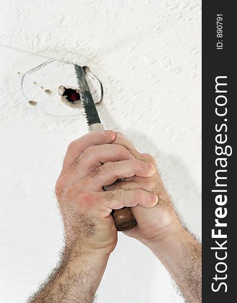 An electrician with using a saw to cut a hole in the ceiling to put a fan box. Work is being performed by a licensed master electrician. An electrician with using a saw to cut a hole in the ceiling to put a fan box. Work is being performed by a licensed master electrician.