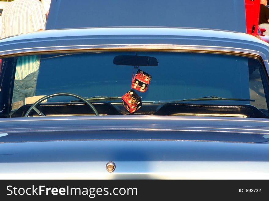 A set of fuzzy red dice hang from the rear view mirror of a Ford Roadster. A set of fuzzy red dice hang from the rear view mirror of a Ford Roadster