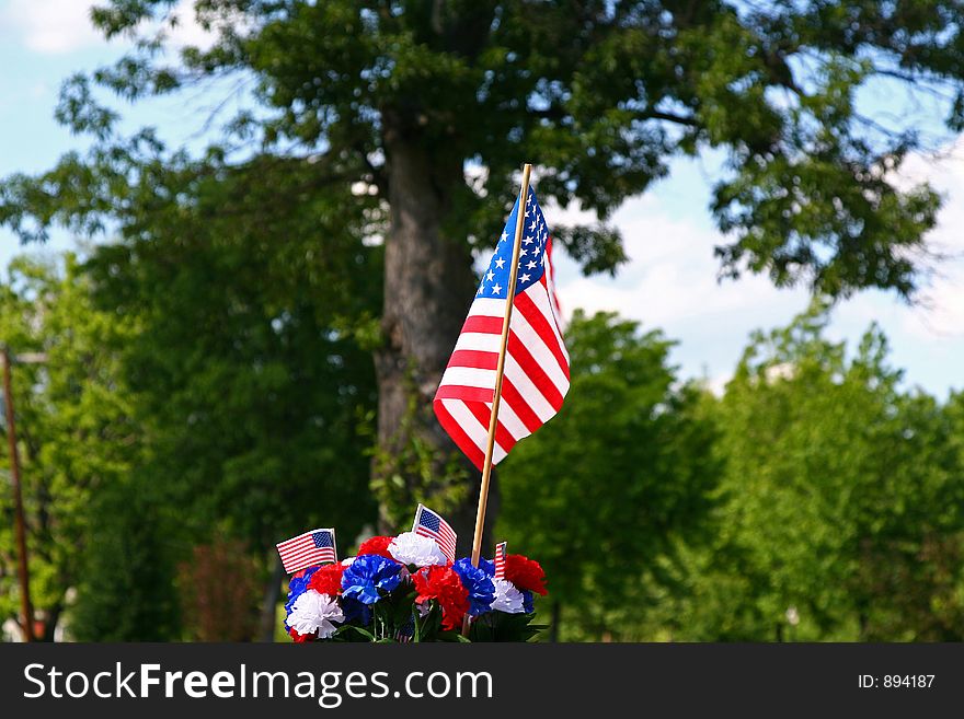 Red, white and blue carnation decoration with American flags in front of a large shade tree. Red, white and blue carnation decoration with American flags in front of a large shade tree