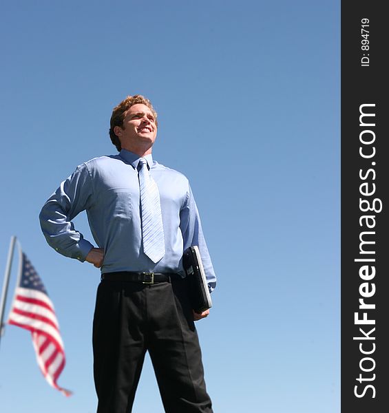 Business man in blue shirt standing in confident pose holding laptop in front of american flag. Business man in blue shirt standing in confident pose holding laptop in front of american flag