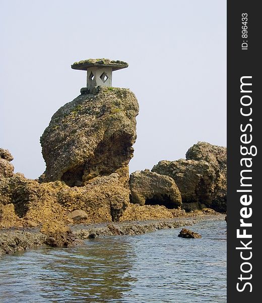 A Japanese stone lantern attached to a rock on the seaside. A Japanese stone lantern attached to a rock on the seaside